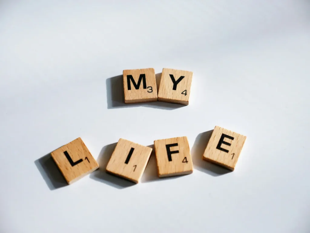 Minimalist lifestyle concept photograph featuring wooden letter tiles that spell out "MY LIFE" on a clean, light background.
