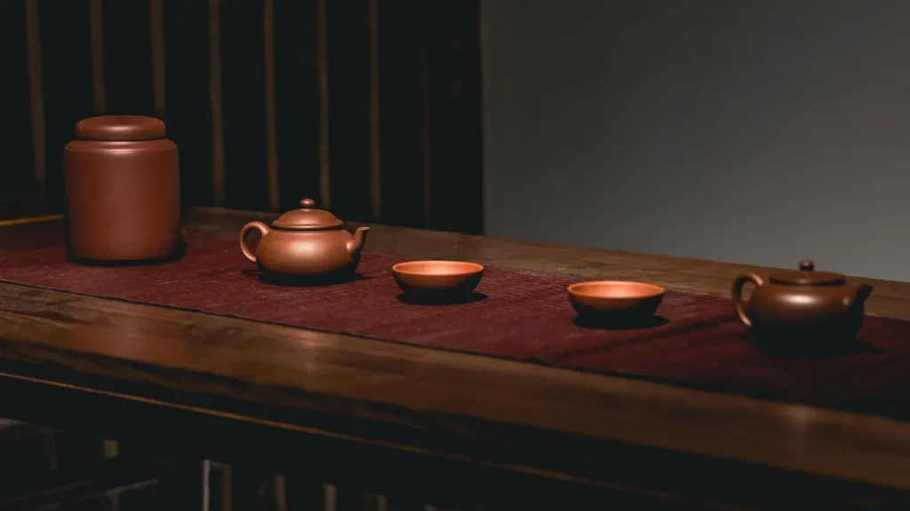 A minimalist gongfu tea table setup with a clay teapot, matching tea cups, and a tea canister on a long wooden table.