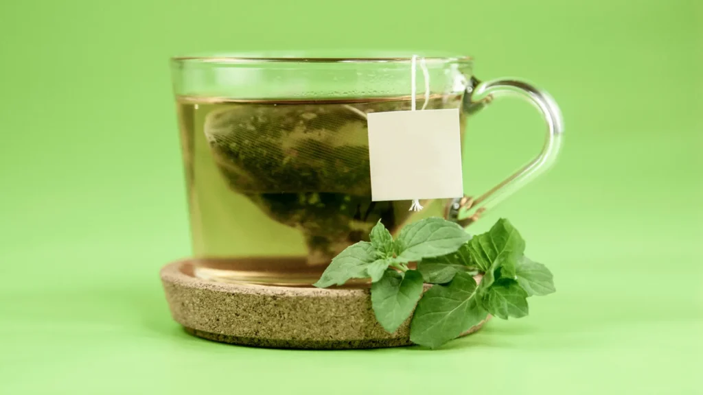 Clear glass mug of green tea with fresh leaves