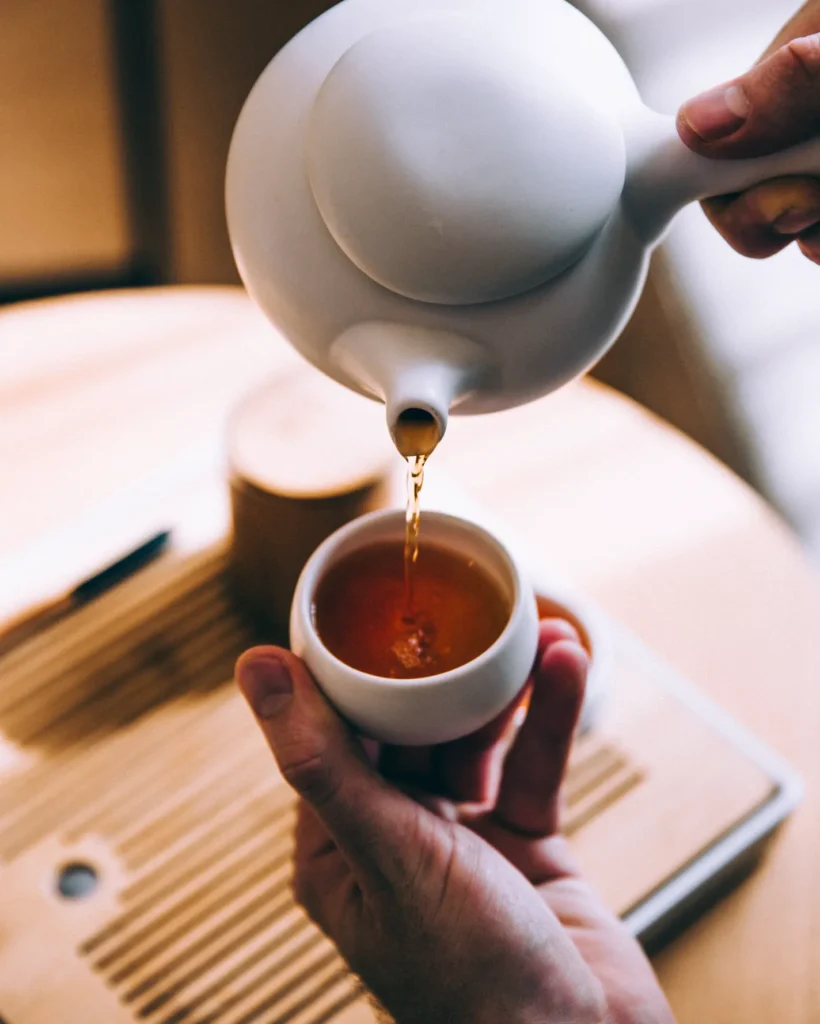 Hands pouring hot tea into a small cup