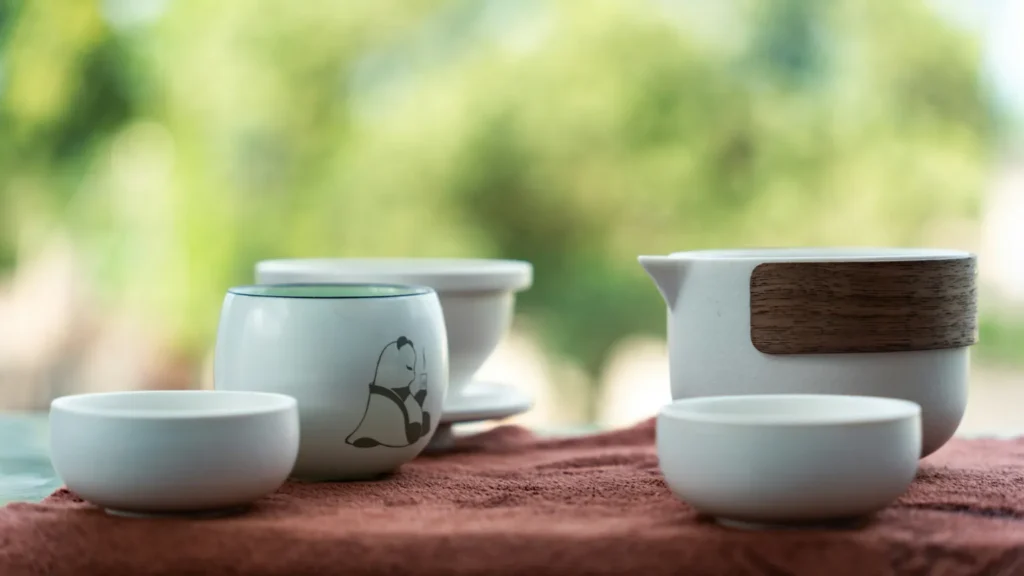 A budget-friendly ceramic gaiwan tea set with a matching fairness cup and small teacups arranged on a tea mat, featuring a clean modern design with subtle panda illustrations.