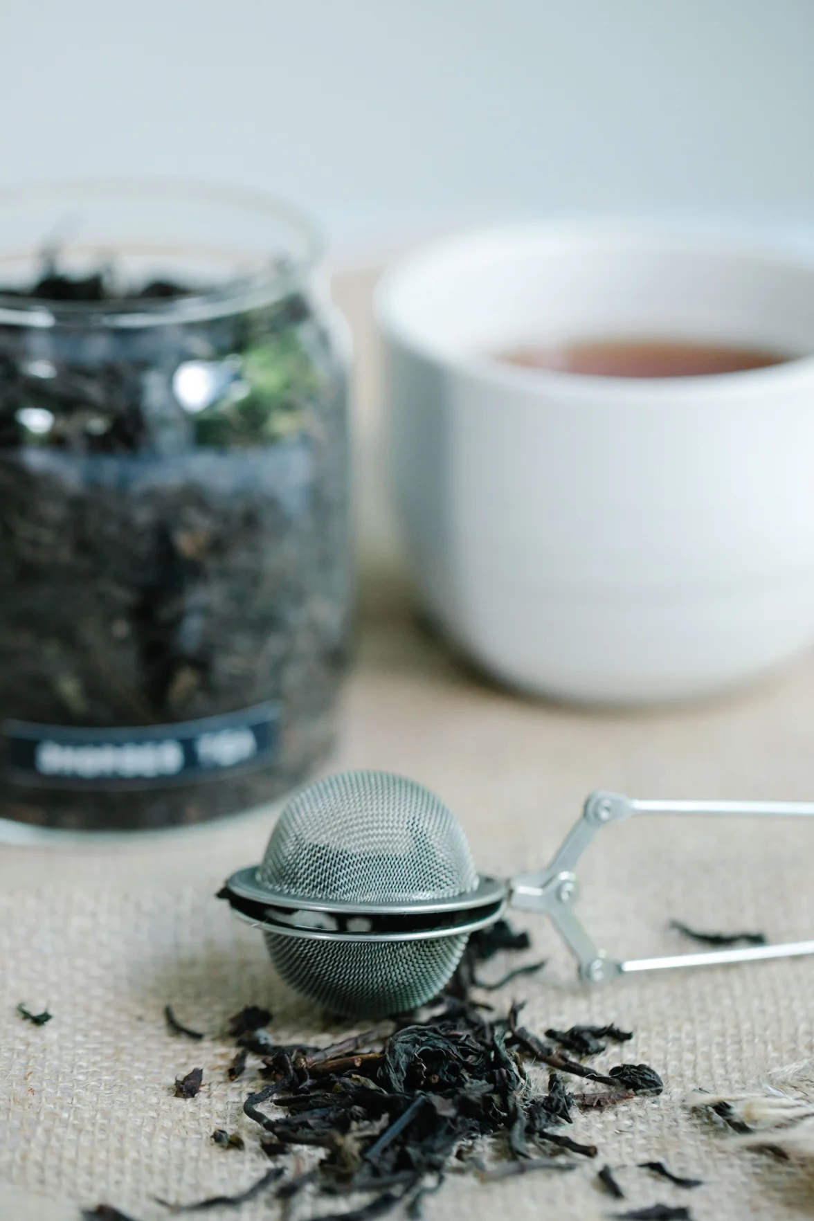 Loose tea leaves beside a tea infuser and jar