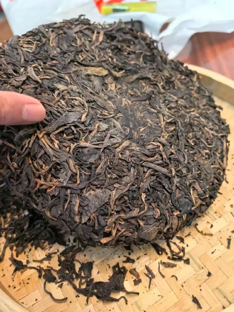 A compressed Chinese shou pu-erh tea cake showing tightly pressed dark brown tea leaves on a wooden surface.